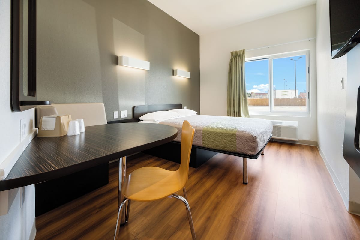 A hotel room with a bed, a desk, a chair, and a window with curtains.