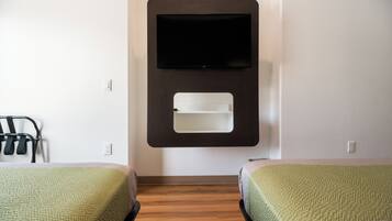 A hotel room with two beds, a TV mounted on the wall, and a small shelf below the TV.