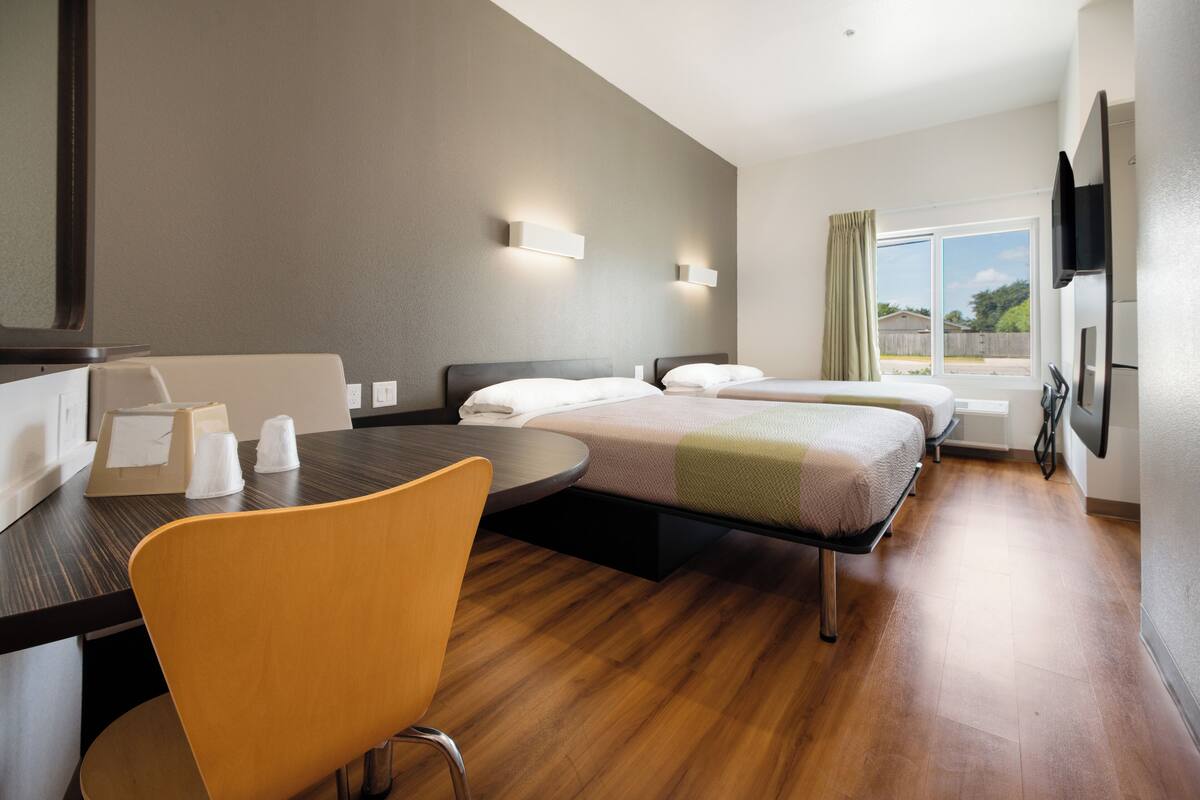 A hotel room with a bed, a desk, a chair, and a window with curtains.