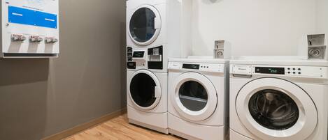 Un espace buanderie comprenant deux machines à laver à chargement frontal superposées, un distributeur mural pour le savon, l’eau de Javel et l’adoucissant, ainsi qu’un sèche-linge de la marque Whirlpool.