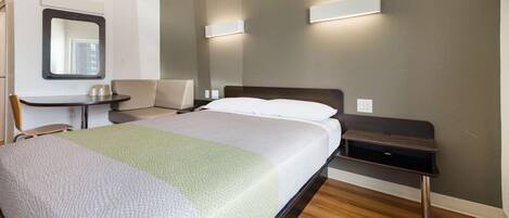 A modern hotel room with a bed, bedside tables, a chair, and a mirror.