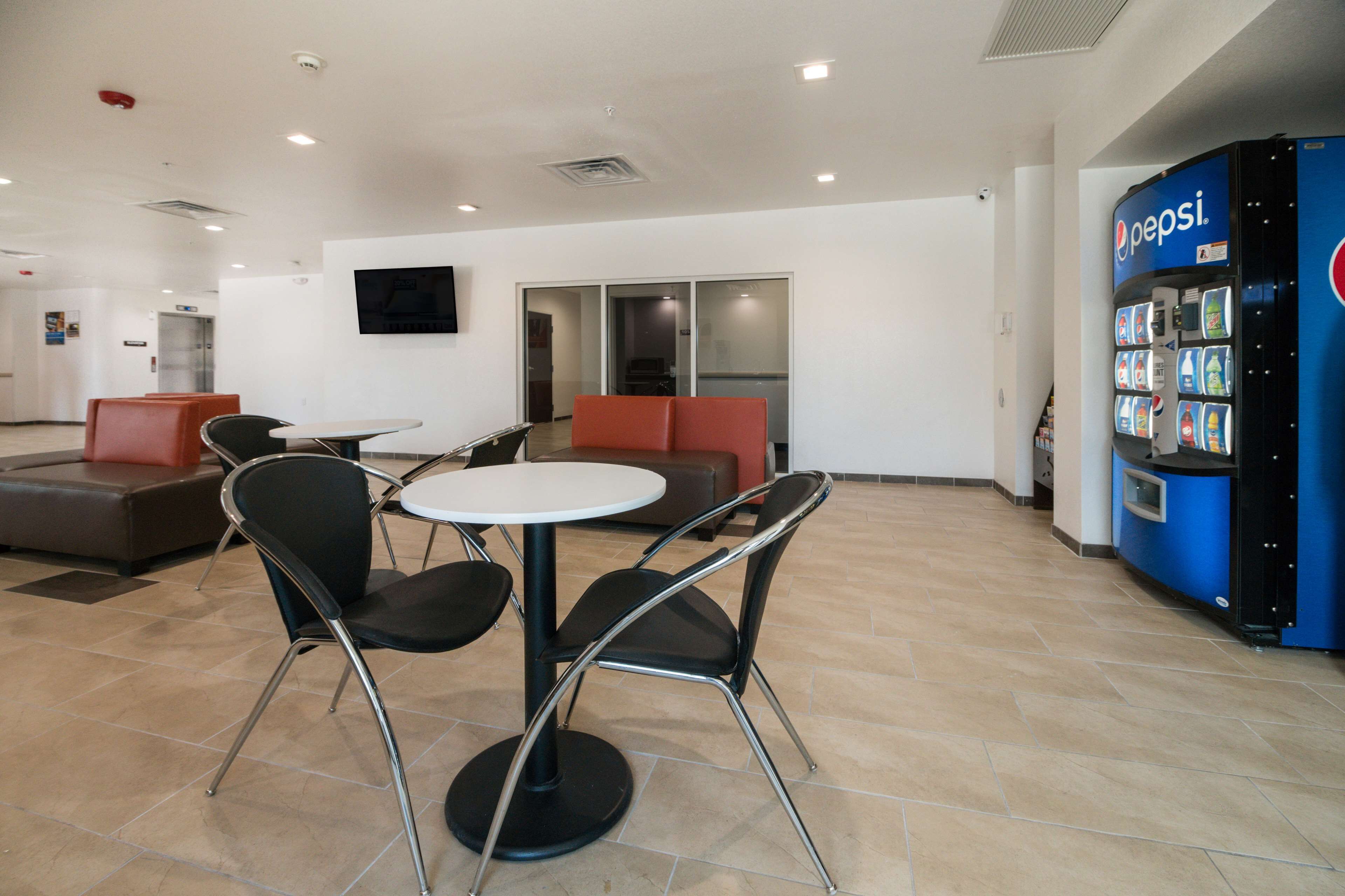 A modern indoor area with a seating arrangement including a round table and chairs, a vending machine, and a television mounted on the wall.