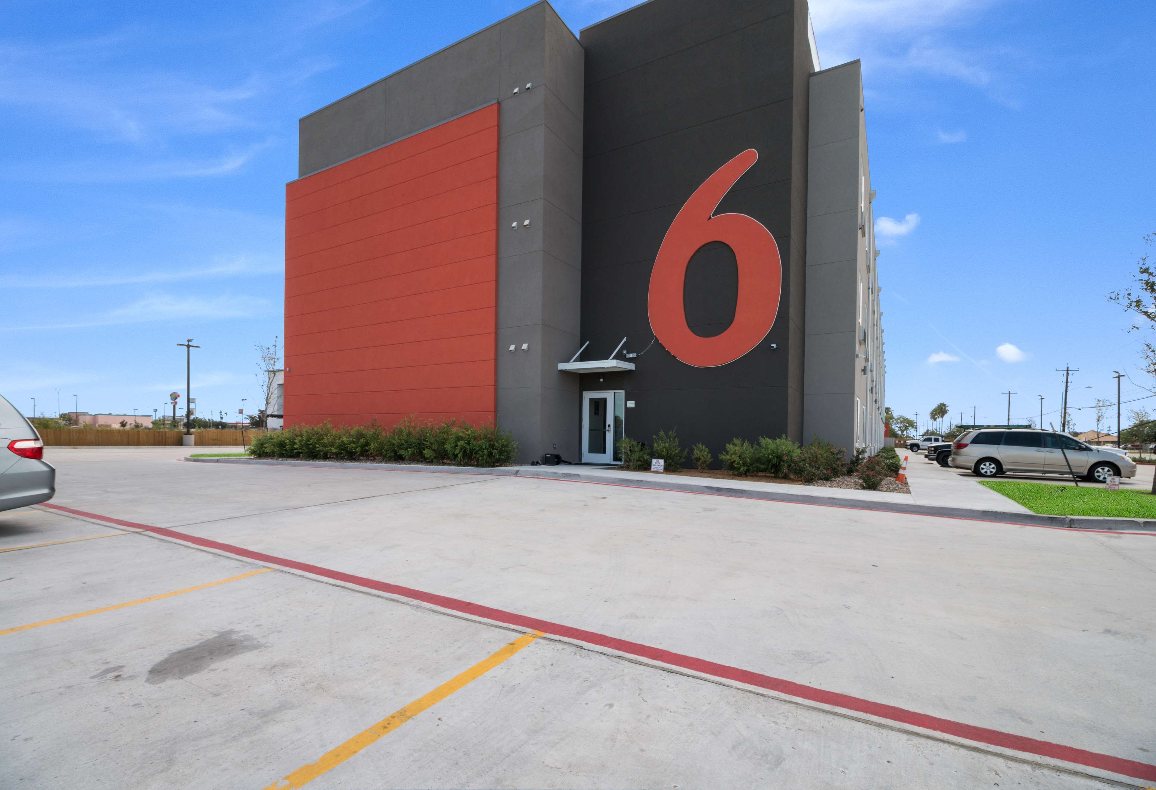 A building with a large red '6' on the side, a parking lot, and a few cars parked nearby.