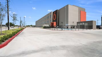 A large building with a prominent '6' sign, a parking lot, and a clear sky.