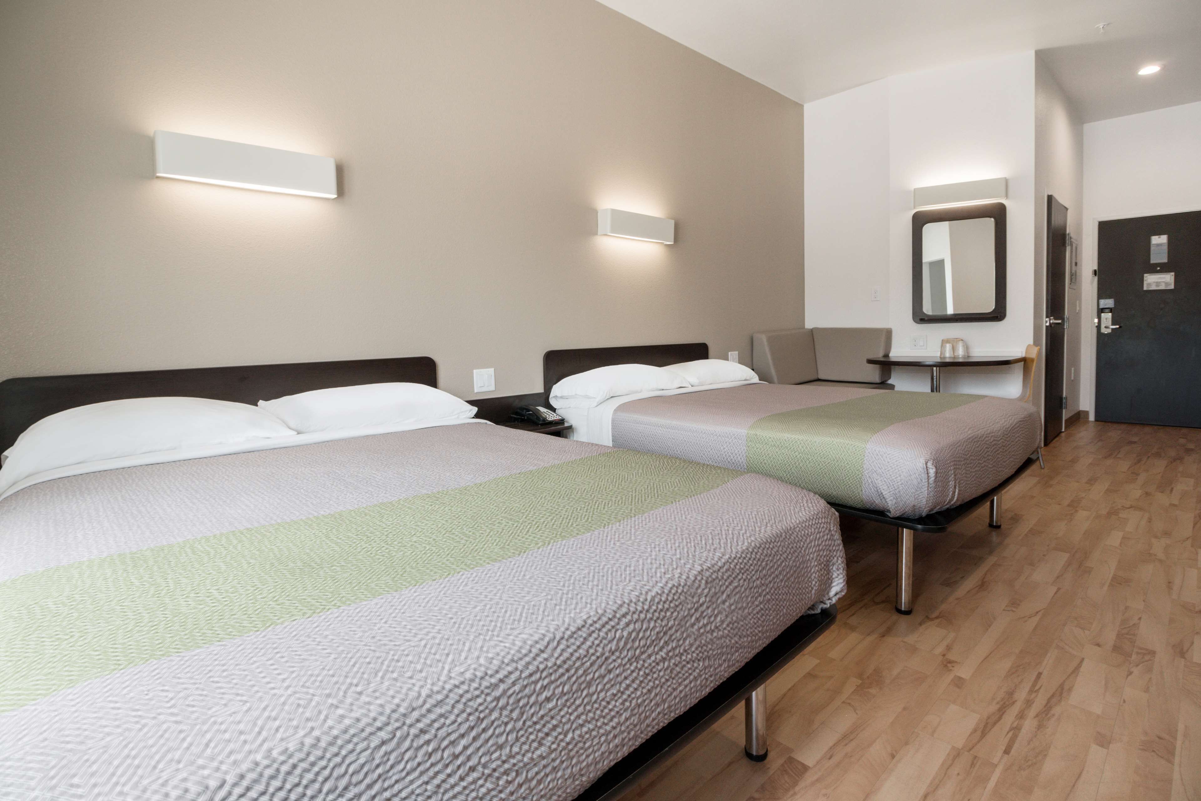 Een hotelkamer met twee bedden, een bureau, een stoel, een spiegel en een deur.