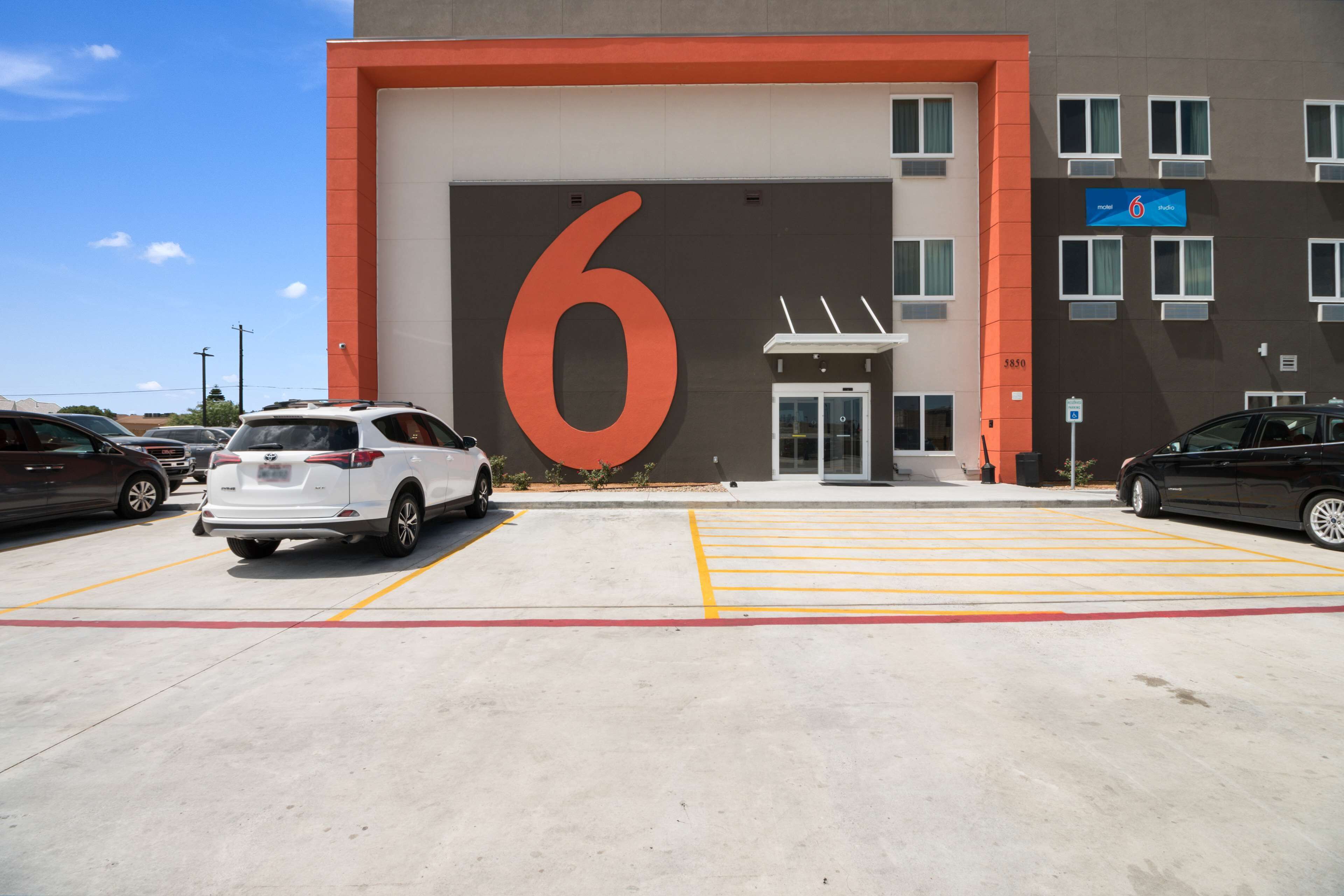 A parking lot with a large '6' sign, a building entrance, and multiple cars parked.