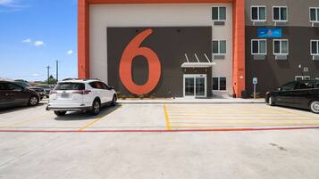 A parking lot with a large '6' sign, a building entrance, and multiple cars parked.