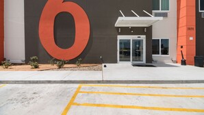 A building entrance with a large '6' sign, a glass door entrance, and a parking lot with yellow lines. - Studio 6 Corpus Christi, TX (Corpus Christi)