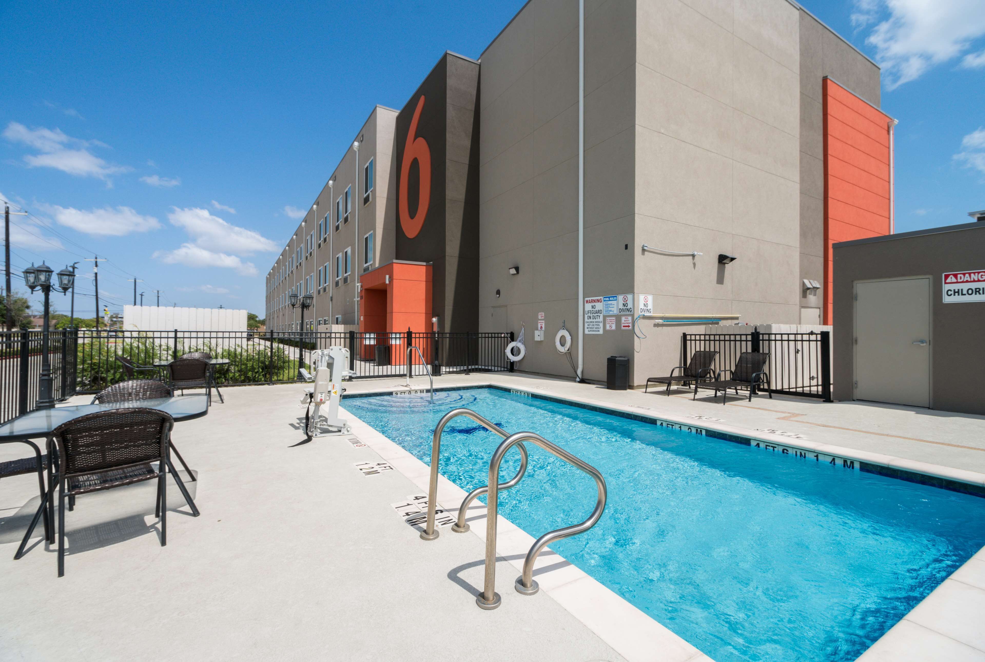 A hotel with a swimming pool, outdoor seating, and a large '6' sign on the building.