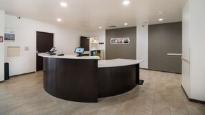 A reception area with a curved reception desk, a computer monitor, and a small shelf with items. - Studio 6 Corpus Christi, TX (Corpus Christi)