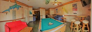 A pool table with a green felt surface, a red sofa, and a ceiling fan.