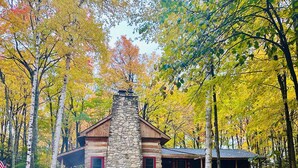 A lodge with a stone chimney, a fire pit, and green Adirondack chairs. - Hand Hewn Log Cabin Newly Renovated, rustic-modern design (Egg Harbor)