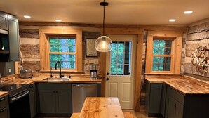 A rustic kitchen with a wooden table, dark cabinets, and large windows. - Hand Hewn Log Cabin Newly Renovated, rustic-modern design (Egg Harbor)