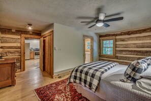 Un dormitorio con una cama, un ventilador de techo, una ventana y una pared de madera.