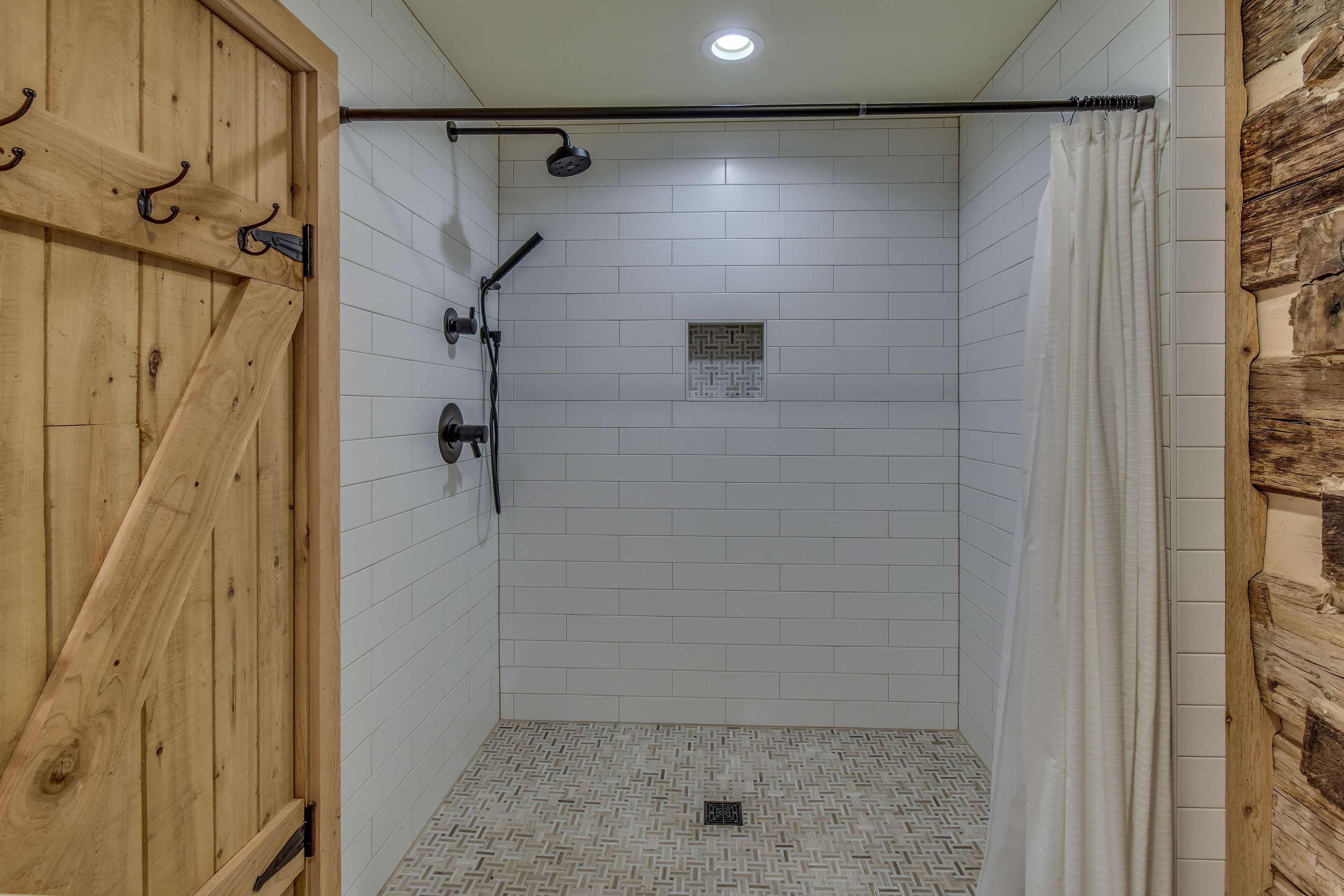 A shower area with a wooden door, white tiled walls, and a patterned floor.