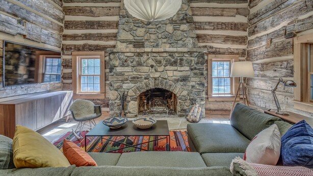 A log cabin interior with a stone fireplace, a sofa, a coffee table, and a television. - Hand Hewn Log Cabin Newly Renovated, rustic-modern design (Egg Harbor)