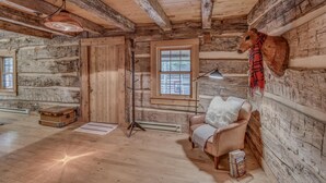 A rustic log cabin interior with a leather armchair, a mounted animal head, and a large window. - Hand Hewn Log Cabin Newly Renovated, rustic-modern design (Egg Harbor)