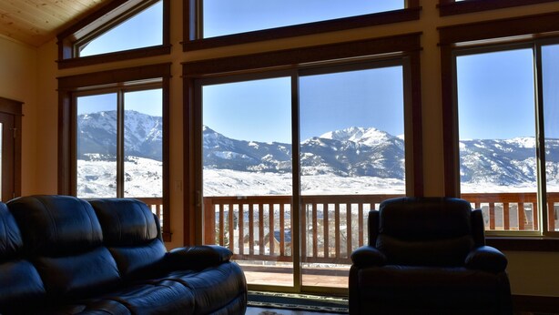 A room with a large window overlooking a snowy mountain landscape. There is a black leather sofa and a black armchair in the room. - Yellowstone Northern Views -- Gorgeous Home. One mile to Yellowstone! (Gardiner)