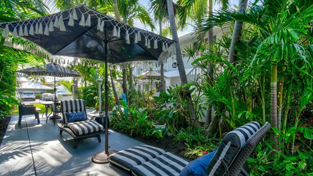 Un espacio al aire libre con asientos tropicales, sillones a rayas, una sombrilla y abundante vegetación.