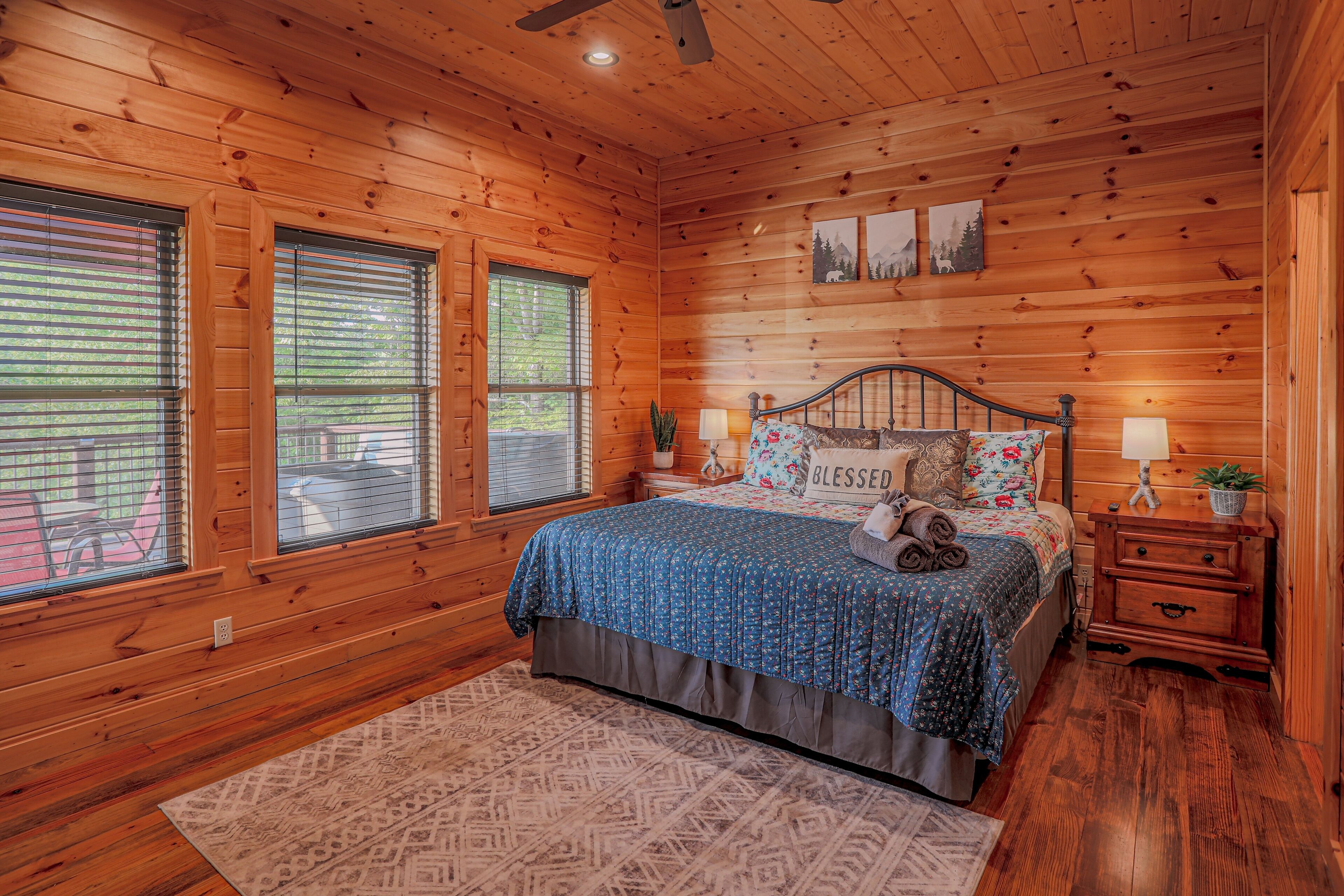 A wooden cabin bedroom with a bed, two bedside lamps, a nightstand, and a window with blinds.