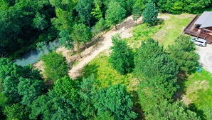 Luftaufnahme eines bewaldeten Gebiets mit einem Feldweg, einer kleinen Holzhütte und einem Fahrzeug.