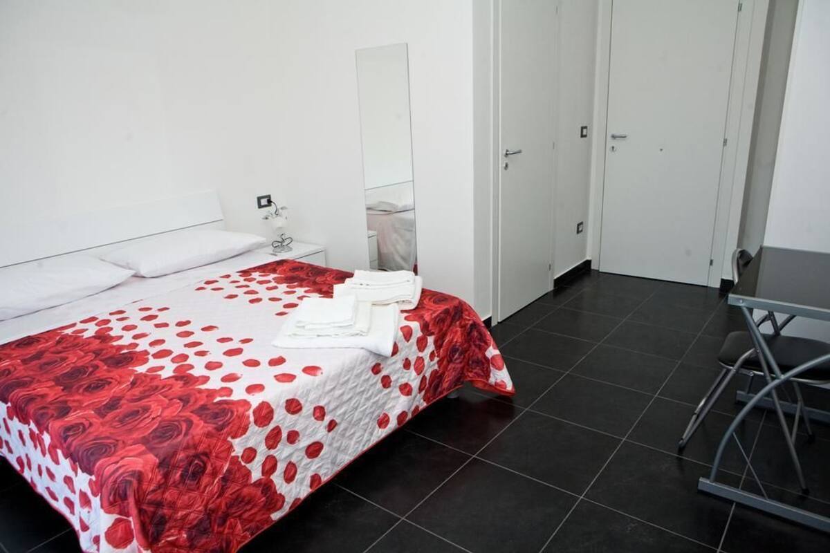 Un dormitorio con cama, mesita de noche, espejo y puerta.