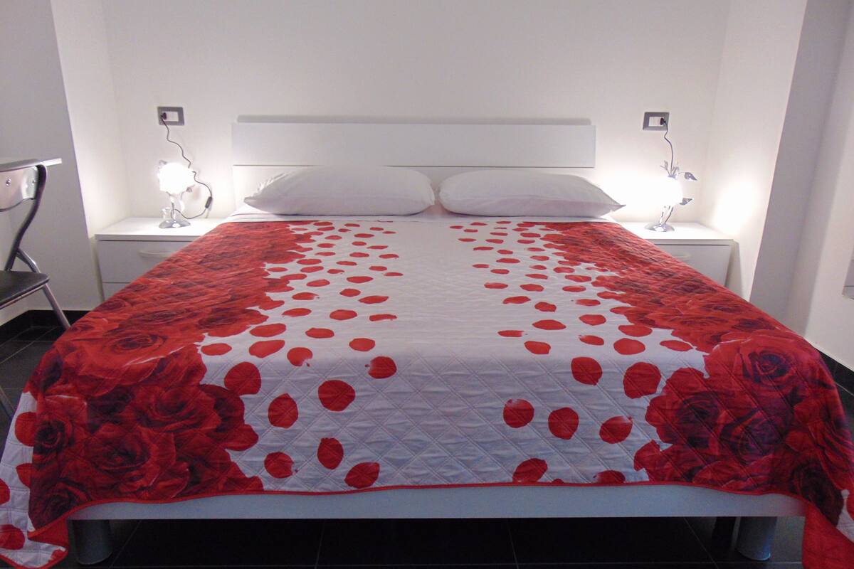 Una cama con cabecera blanca y colcha estampada de flores rojas y blancas.