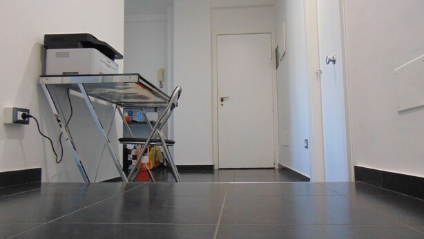 A hallway with a glass-top desk, a closed door, and a tiled floor. - B&B Etna's Tourist (Catania)