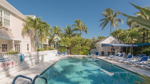 A pool area with clear blue water, lounge chairs, and palm trees.