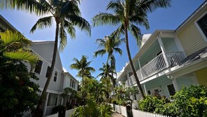 A row of white colonial-style buildings with balconies, surrounded by palm trees and a white picket fence.