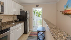 A kitchen with white cabinets, stainless steel appliances, a granite countertop, and a colorful striped rug.