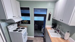 A compact kitchen with white cabinets, a stove, a sink, and a window with blinds. - Warm Springs Retreat (Warm Springs)