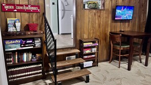 A cozy room with a wooden playroom sign, a bookshelf with board games, a small table with a chair, and a television displaying a sports event. - Warm Springs Retreat (Warm Springs)