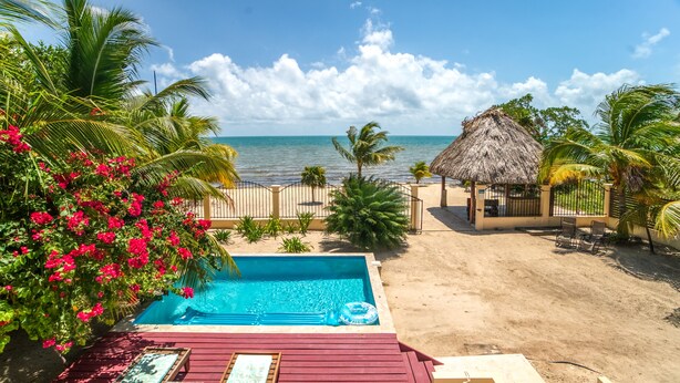 A pool with a wooden deck, a thatched-roof structure, and a beach view. - Beachfront Villa • Private Pool • Fully Fenced • Walk to Restaurants (Placencia)