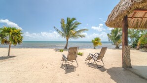 A beach with two lounge chairs and a thatched-roof structure. - Beachfront Villa • Private Pool • Fully Fenced • Walk to Restaurants (Placencia)