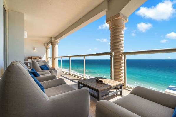 A balcony with a view of the ocean, furnished with sofas and a table.
