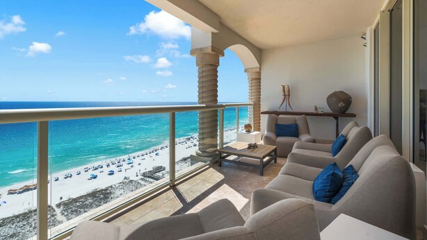 A balcony with a view of the beach, a sofa with blue cushions, and a small table.