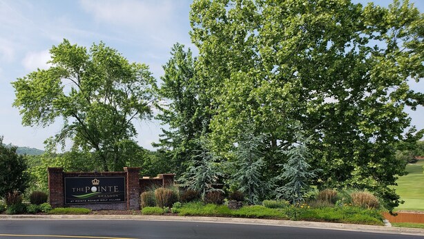 Schild für The Pointe in Pointe Royale Golf Village, mit Ziegelmauer und umlaufendem Grün.