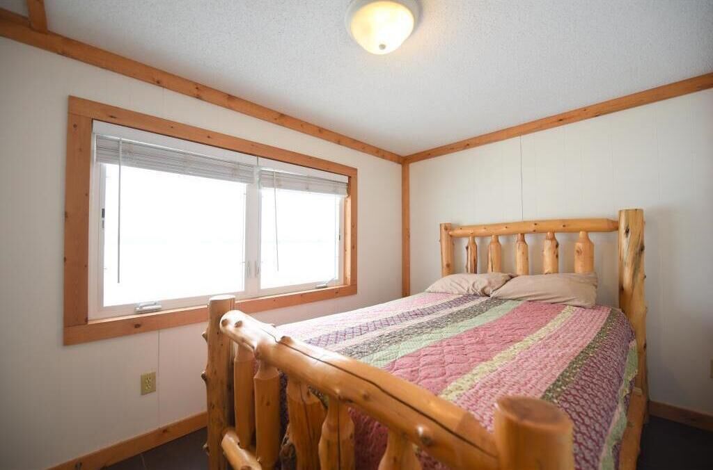 Un dormitorio con estructura de cama de madera, una ventana con persianas y una lámpara en el techo.
