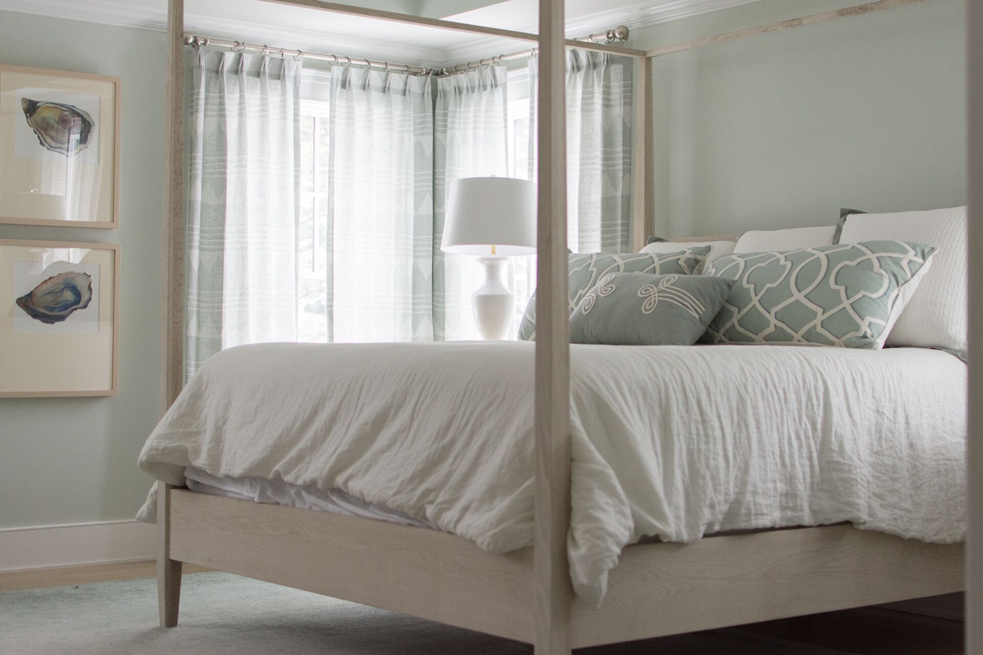 A bedroom with a four-poster bed, a bedside table with a lamp, and two framed pictures on the wall.
