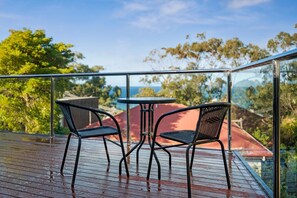 Un balcon avec deux chaises et une table, d’où l’on peut admirer un bâtiment aux toits rouges et des arbres.