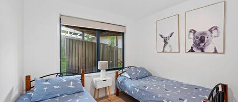 A bedroom with two single beds, a small desk, a chair, and two framed pictures on the wall.