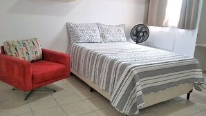 A bedroom with a bed, a red chair, a bedside fan, and shelves with decorative items. - Casa Maceio Shopping (Maceió)