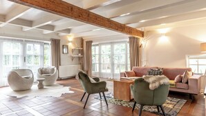 A spacious living room with a high ceiling, large windows, and a mix of modern and classic furniture.