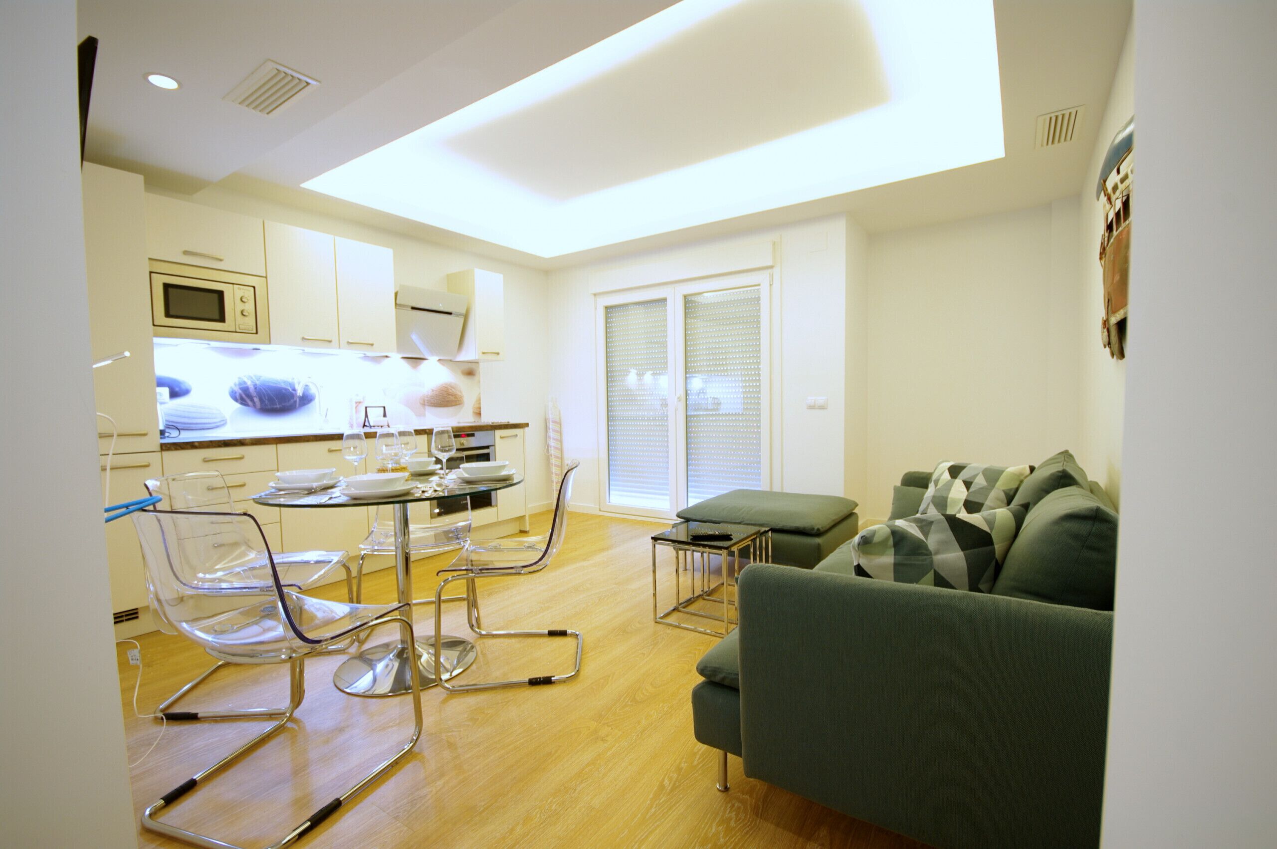 A modern kitchen with a dining area, a sofa, and a large window.