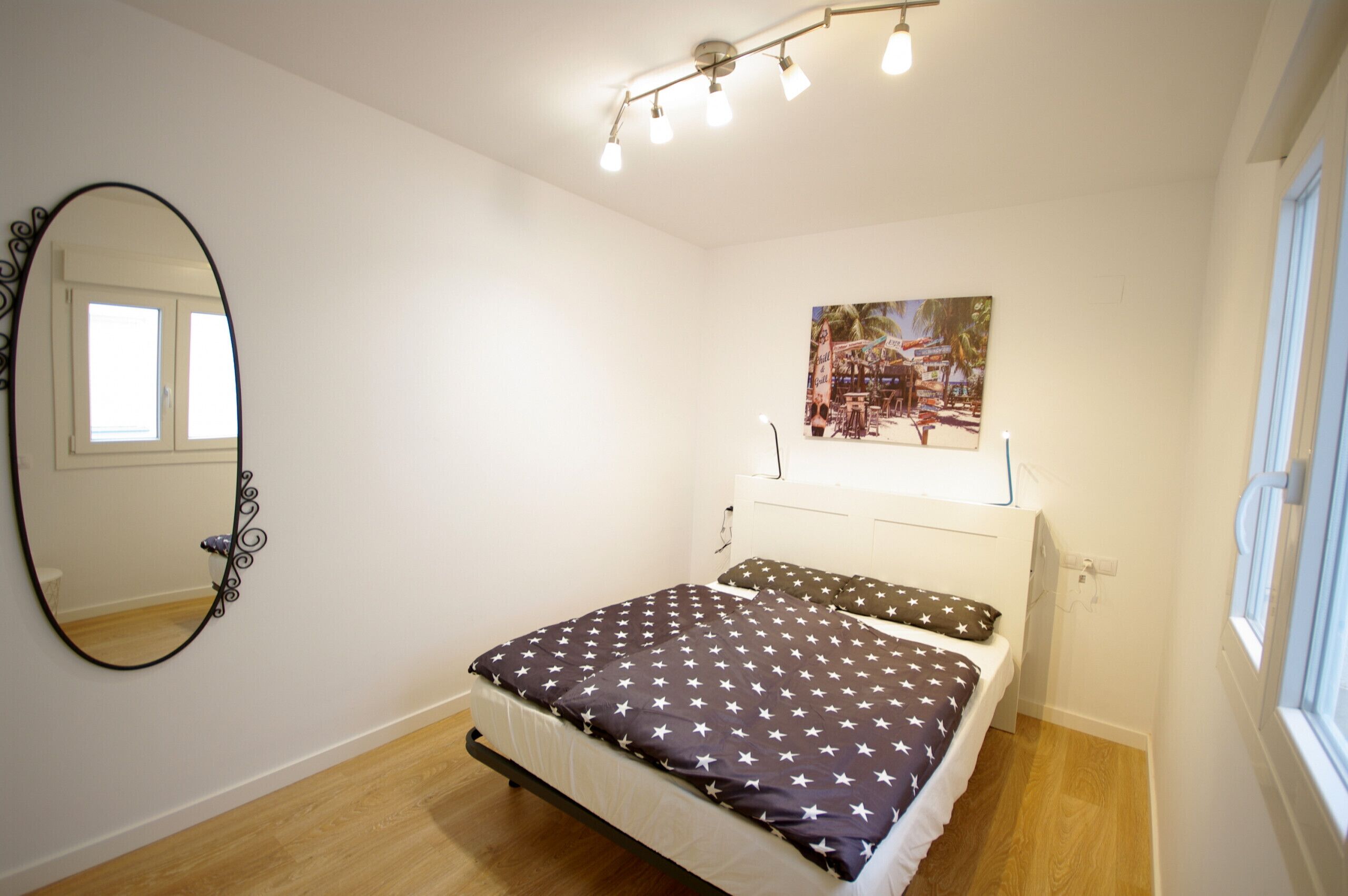 Une chambre à coucher comprenant un lit, un grand miroir, un luminaire au plafond et un tableau accroché au mur.