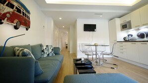 A modern living room with a sofa, a dining table with chairs, a kitchen area with cabinets and a microwave, and a mounted TV. - 29 - Livingtarifa Ventura Levante (Tarifa)