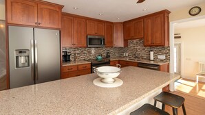 A kitchen with wooden cabinets, a stainless steel refrigerator, a microwave, a stove, and a granite countertop. - The North Star of Honeoye: Family Friendly, Great View of Honeoye Lake! (Honeoye)