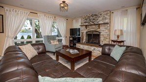 A living room with leather sofas, a stone fireplace, a television, and a view of the outdoors. - The North Star of Honeoye: Family Friendly, Great View of Honeoye Lake! (Honeoye)