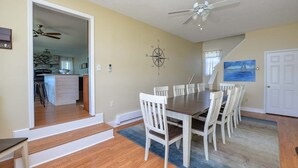 A dining area with a large table and chairs, a ceiling fan, and a kitchen visible through an open doorway. - The North Star of Honeoye: Family Friendly, Great View of Honeoye Lake! (Honeoye)